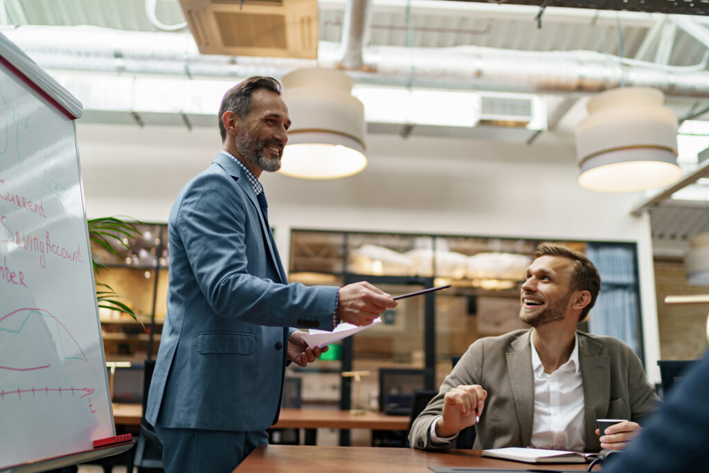 Mature business coach or speaker make flip chart presentation to diverse businesspeople at meeting